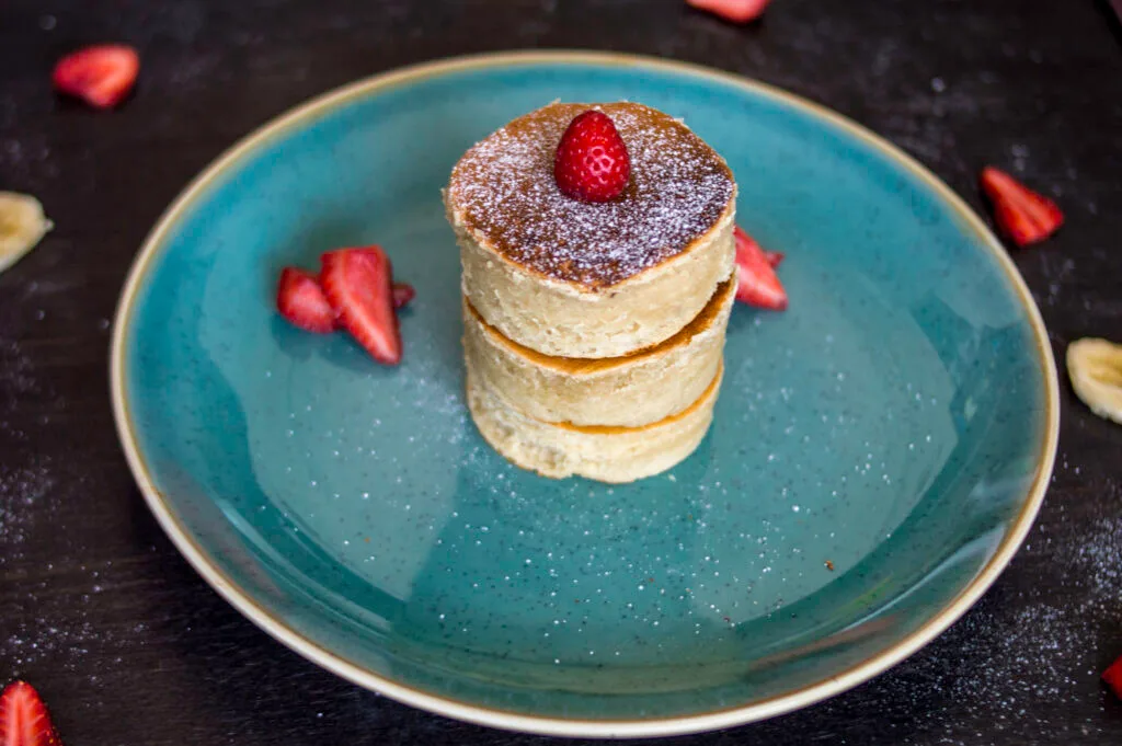 Stack of fluffy vegan Japanese pancakes topped with powdered sugar and fresh berries on a white plate