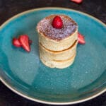 Stack of fluffy vegan Japanese pancakes topped with powdered sugar and fresh berries on a white plate