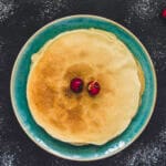 Stack of golden vegan crêpes with fresh fruit and maple syrup on top