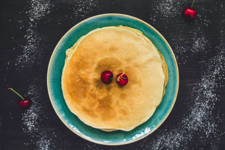 Stack of golden vegan crêpes with fresh fruit and maple syrup on top