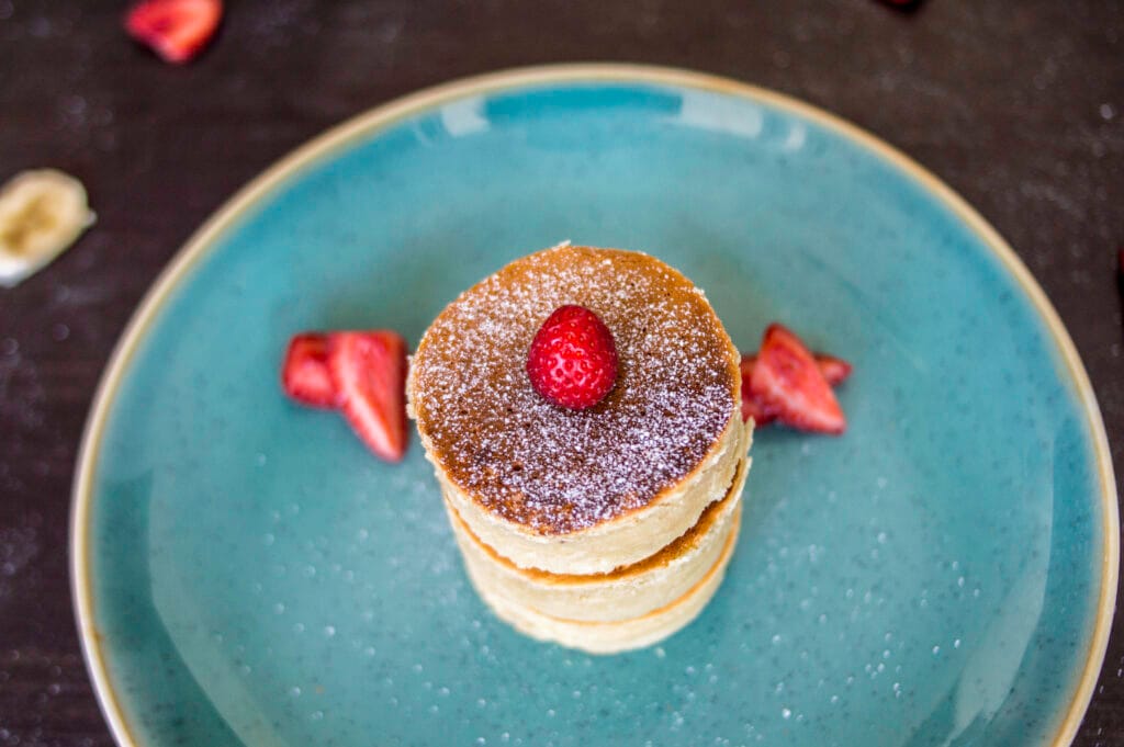 Stack of fluffy vegan Japanese pancakes topped with powdered sugar and fresh berries on a white plate