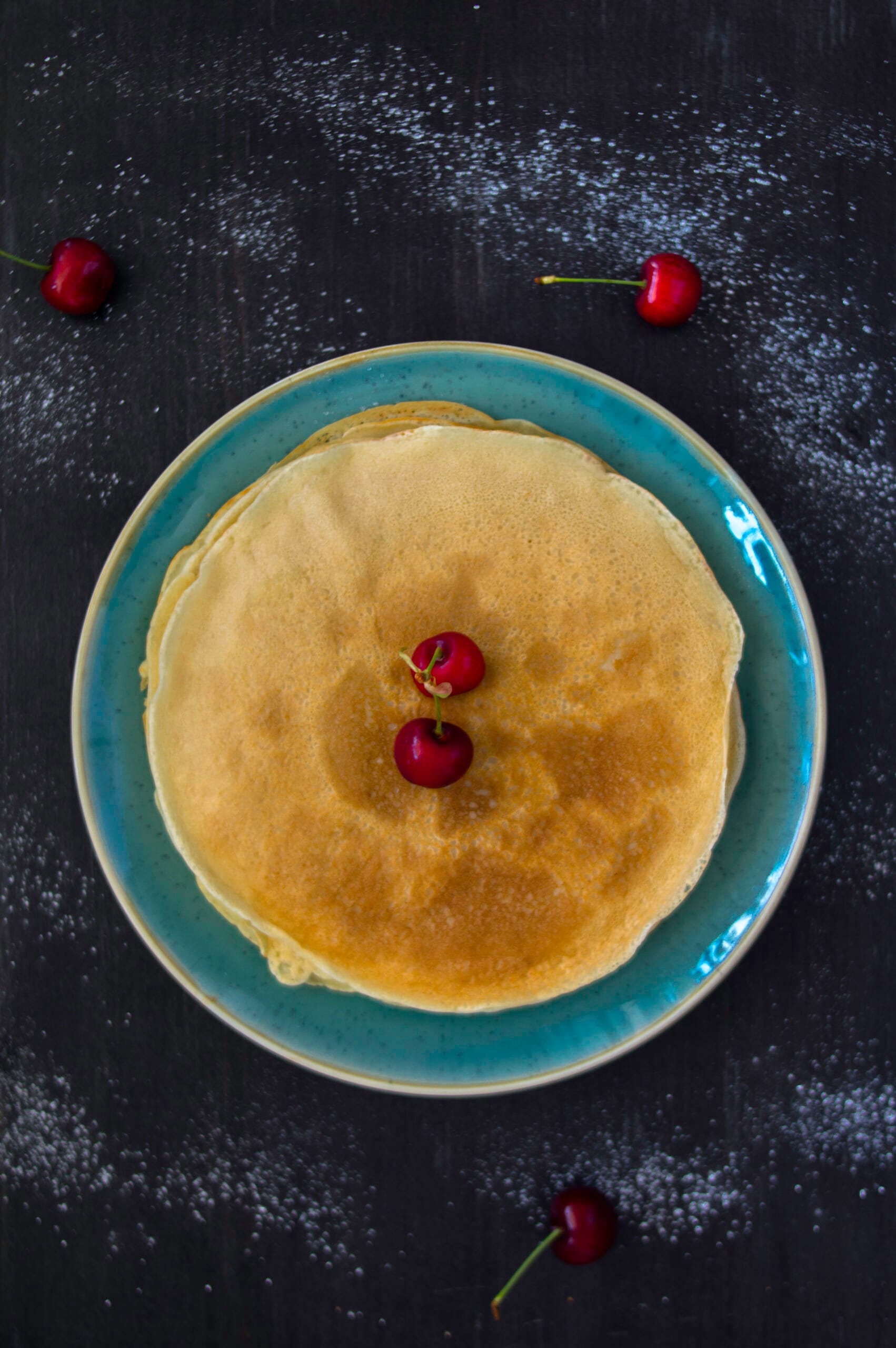Stack of golden vegan crêpes with fresh fruit and maple syrup on top