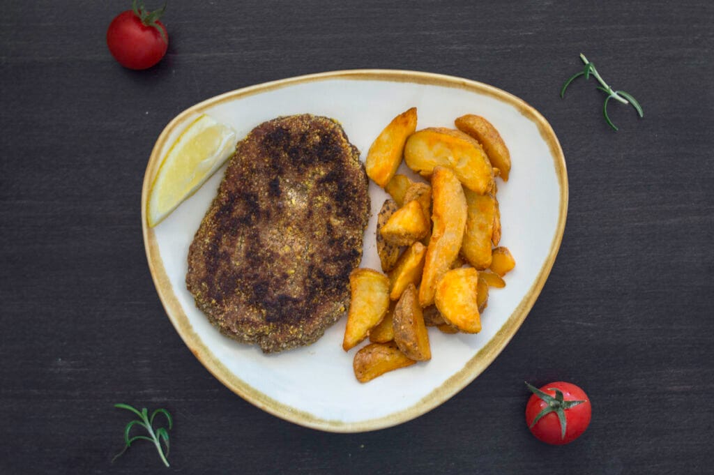 Crispy golden vegan schnitzels served with fries and lemon wedges on a rustic plate