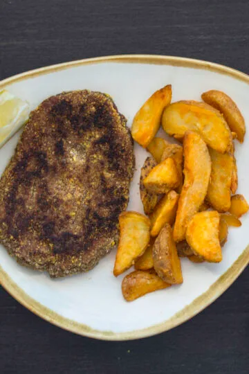 Crispy golden vegan schnitzels served with fries and lemon wedges on a rustic plate