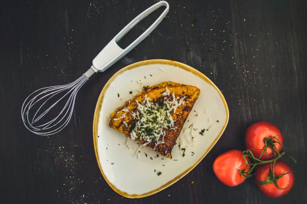 Sliced vegan chickpea omelette on a plate with herbs and side salad