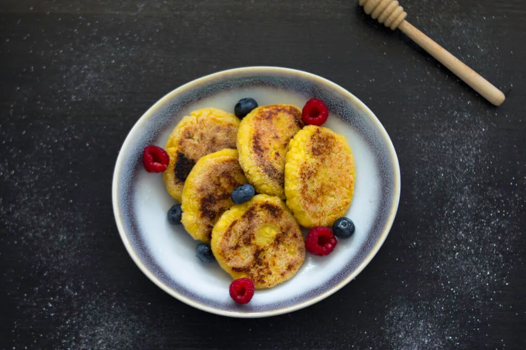 Stack of golden vegan cottage cheese pancakes (Syrniki) with a dusting of powdered sugar and fresh berries on top