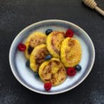 Stack of golden vegan cottage cheese pancakes (Syrniki) with a dusting of powdered sugar and fresh berries on top