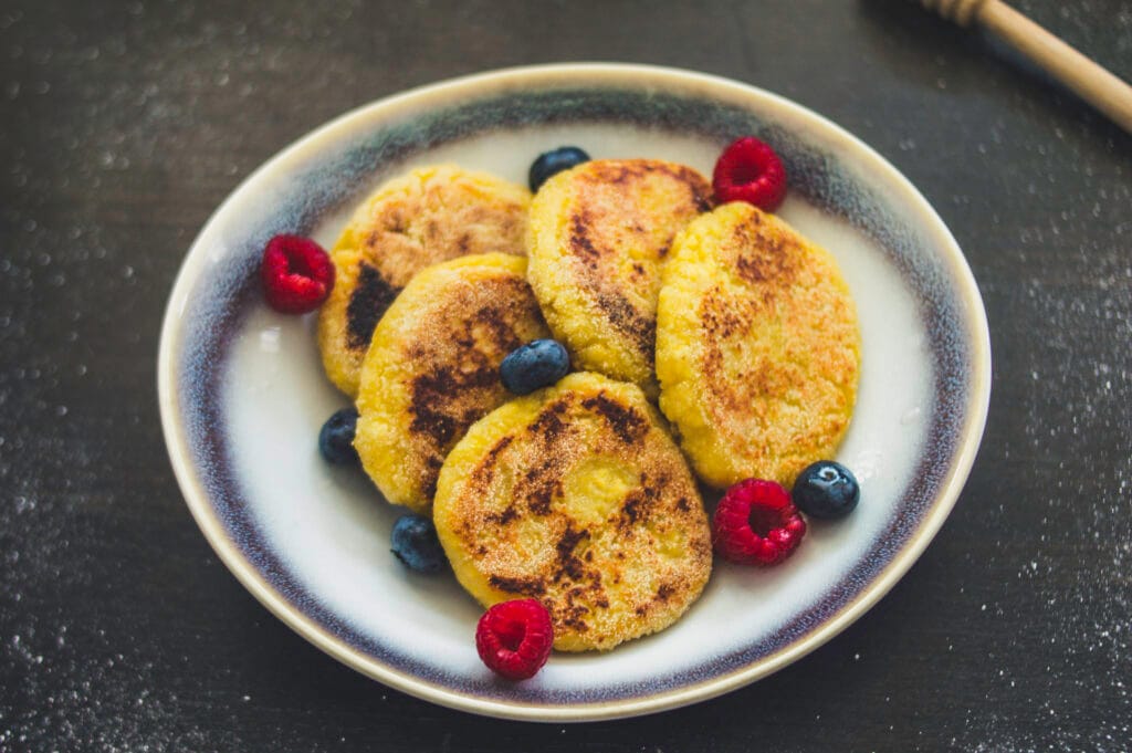 Stack of golden vegan cottage cheese pancakes (Syrniki) with a dusting of powdered sugar and fresh berries on top