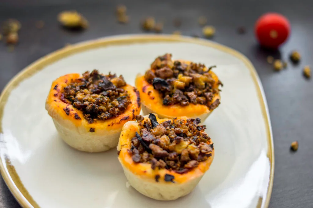 Baked vegan pizza-tofu baskets in muffin tin, topped with herbs and tomato sauce