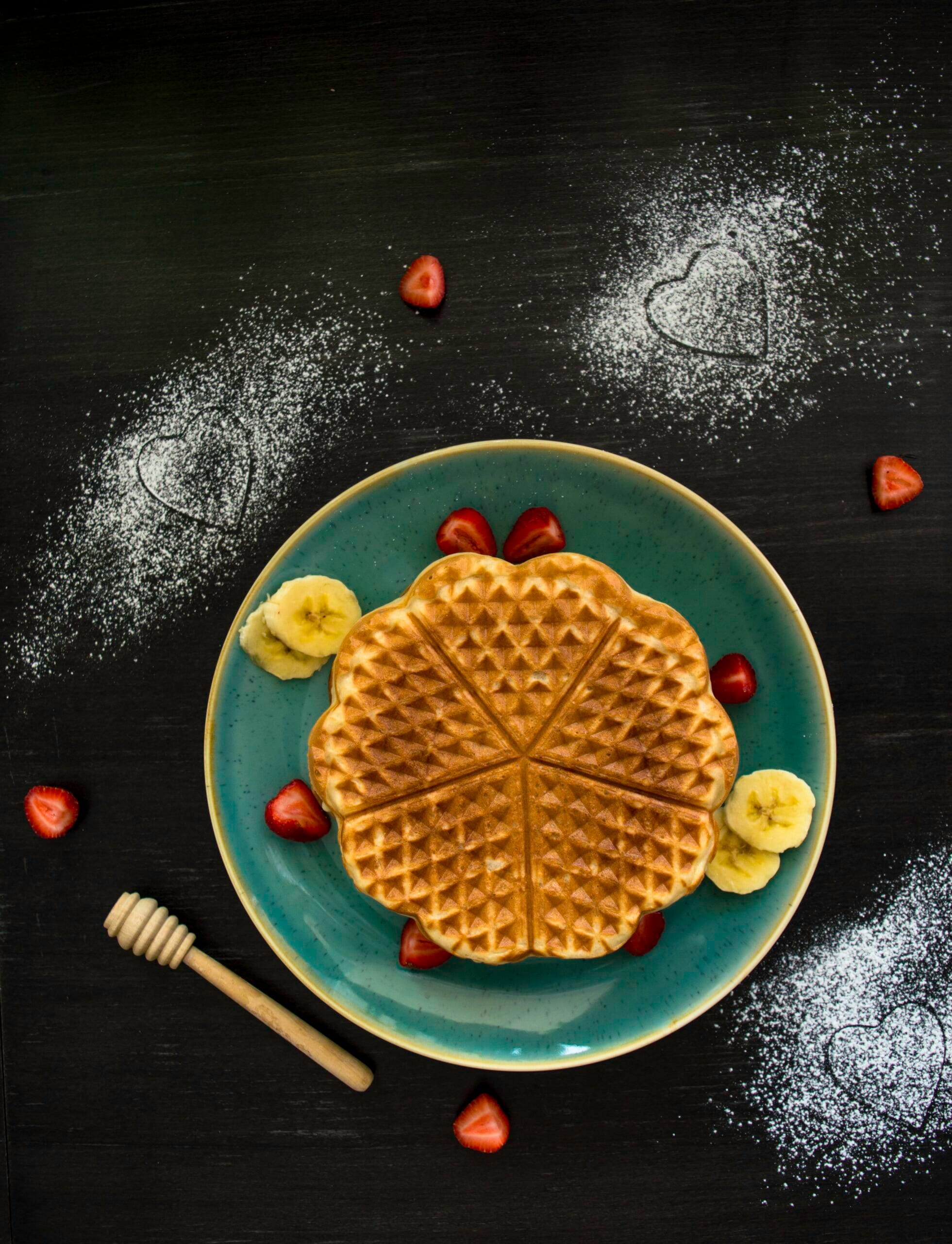 Stack of fluffy vegan Belgian waffles topped with syrup and berries on a white plate