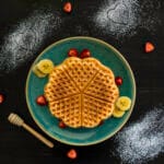 Stack of fluffy vegan Belgian waffles topped with syrup and berries on a white plate