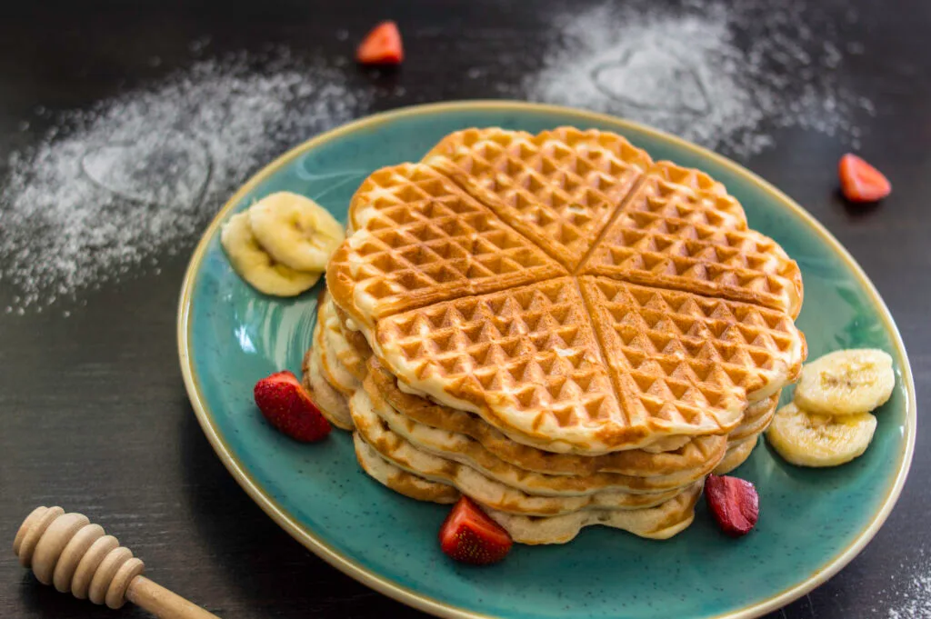 Stack of fluffy vegan Belgian waffles topped with syrup and berries on a white plate