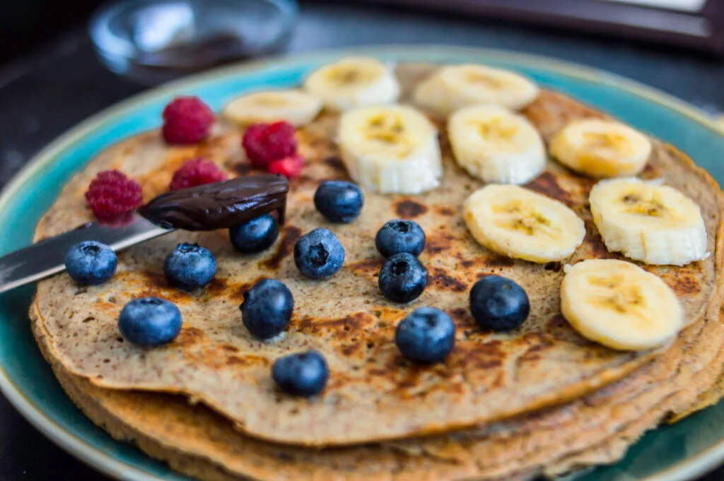 Stack of thick, golden brown fluffy crepes with flaxseed served with berries and vegan yogurt on a rustic plate