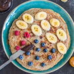 Stack of thick, golden brown crepes served with berries and vegan yogurt on a rustic plate