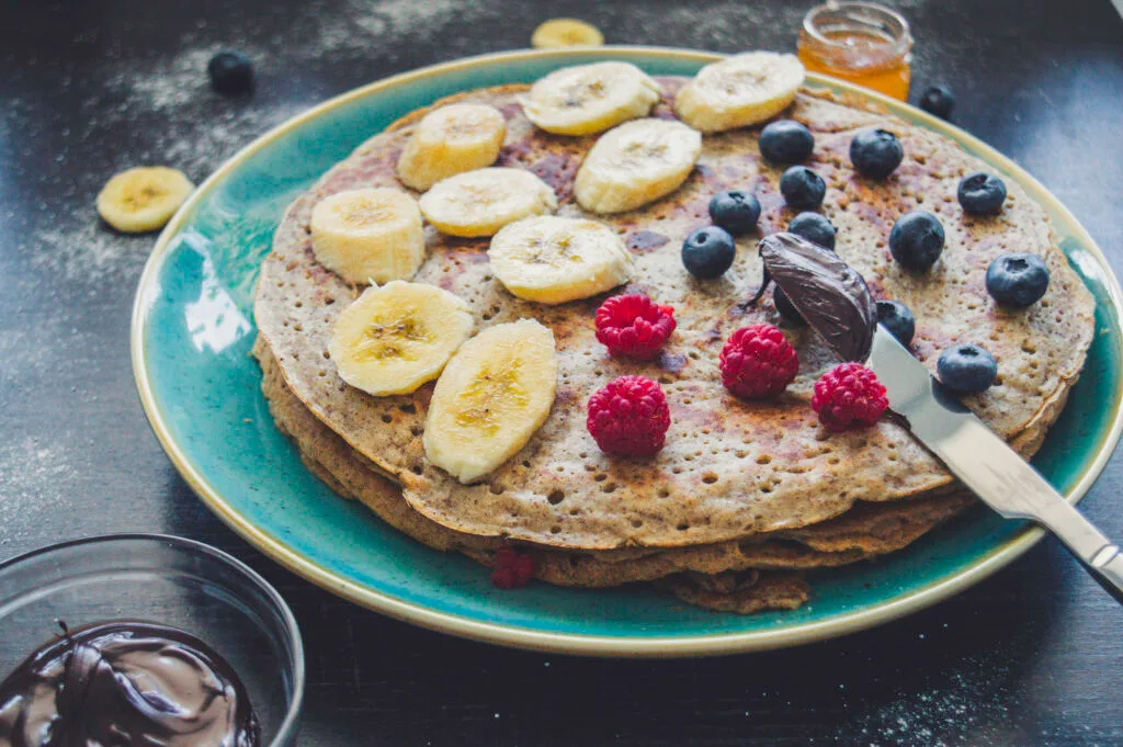 Stack of thick, golden brown  fluffy crepes with flaxseed served with berries and vegan yogurt on a rustic plate