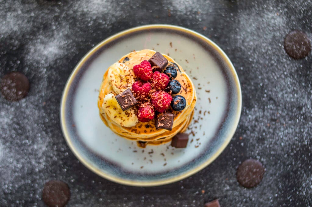 Stack of fluffy banana-chocolate chip pancakes topped with syrup and banana slices on a plate