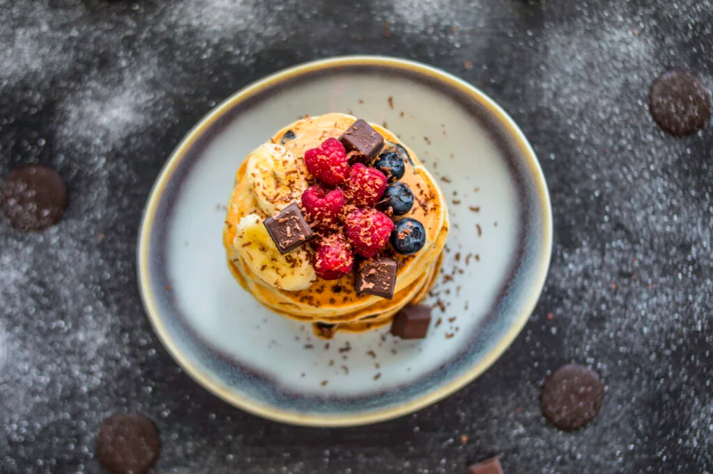 Stack of fluffy banana-chocolate chip pancakes topped with syrup and banana slices on a plate