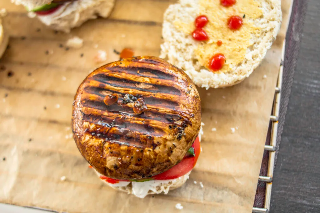 Grilled mushroom burger stacked with tomato, cucumber, and sauce on a toasted vegan bun