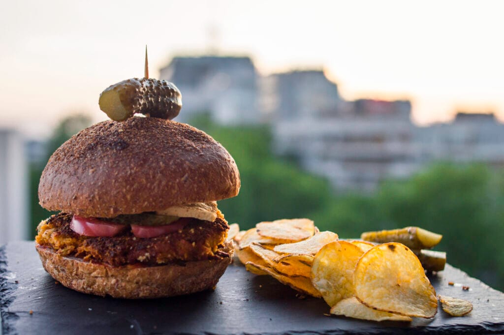 Crispy curry chickpea burger patty on a toasted bun with lettuce, tomato, and vegan mayo served with sweet potato fries