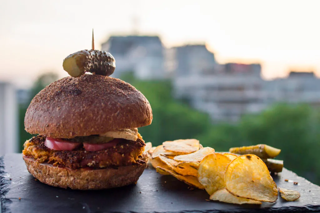 Crispy curry chickpea burger patty on a toasted bun with lettuce, tomato, and vegan mayo served with sweet potato fries