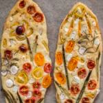 Artistic garden focaccia topped with tomatoes, bell peppers, spring onions, and herbs on a golden crust
