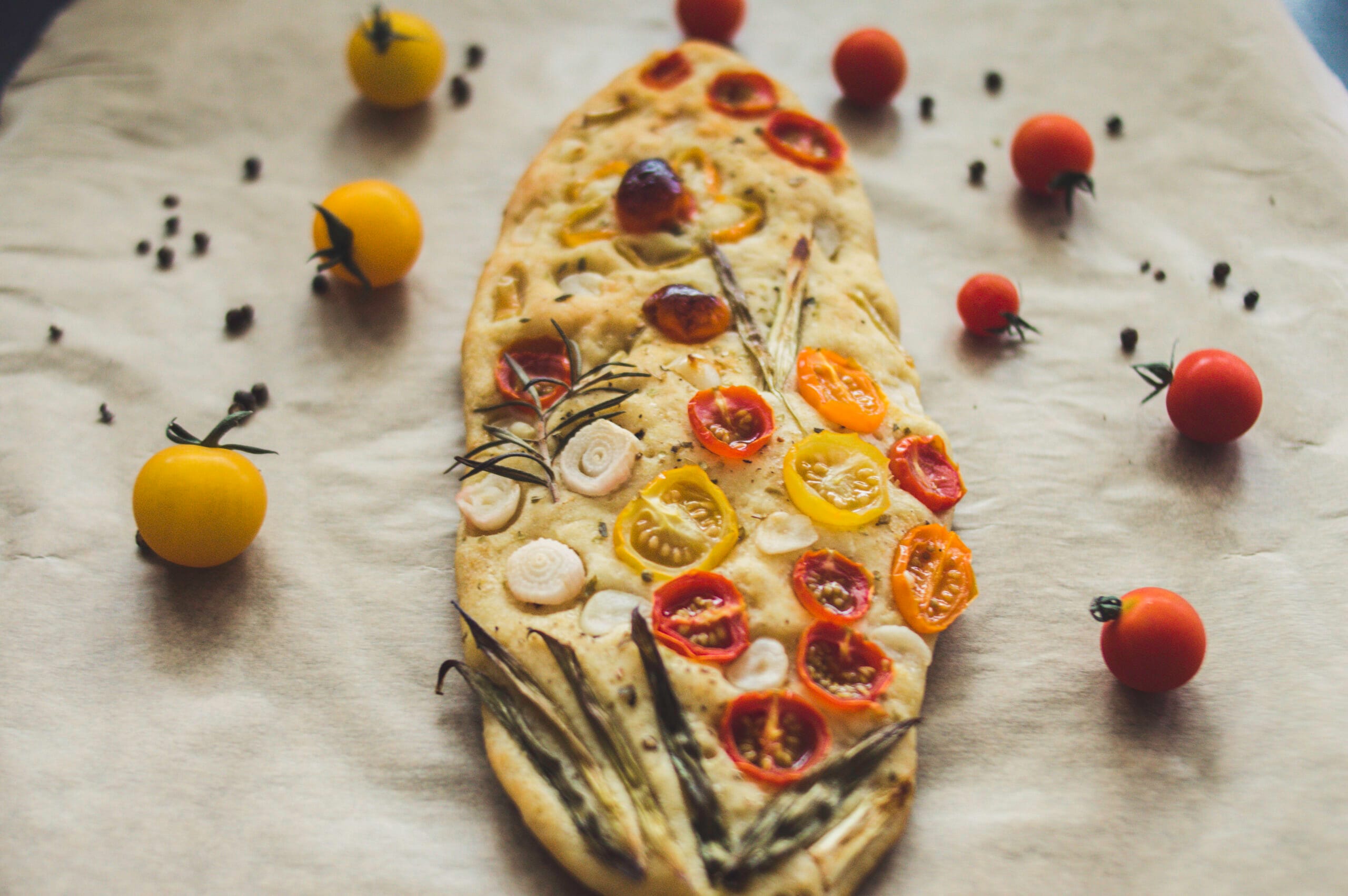 Artistic garden focaccia topped with tomatoes, bell peppers, spring onions, and herbs on a golden crust