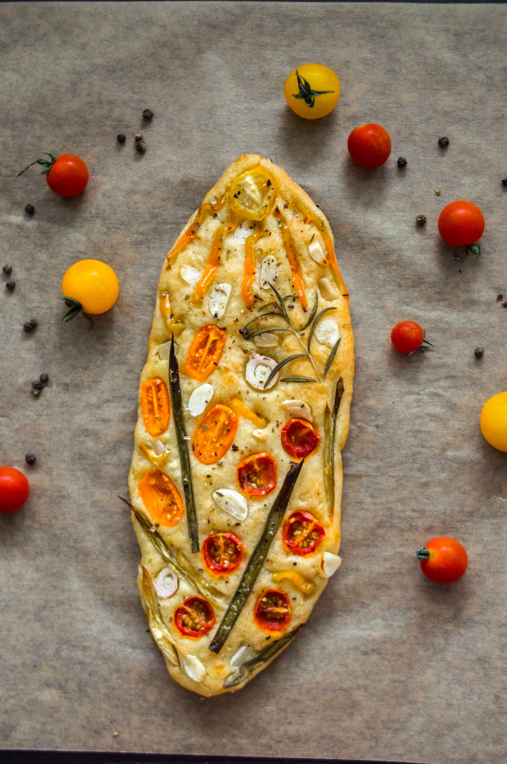 Artistic garden focaccia topped with tomatoes, bell peppers, spring onions, and herbs on a golden crust