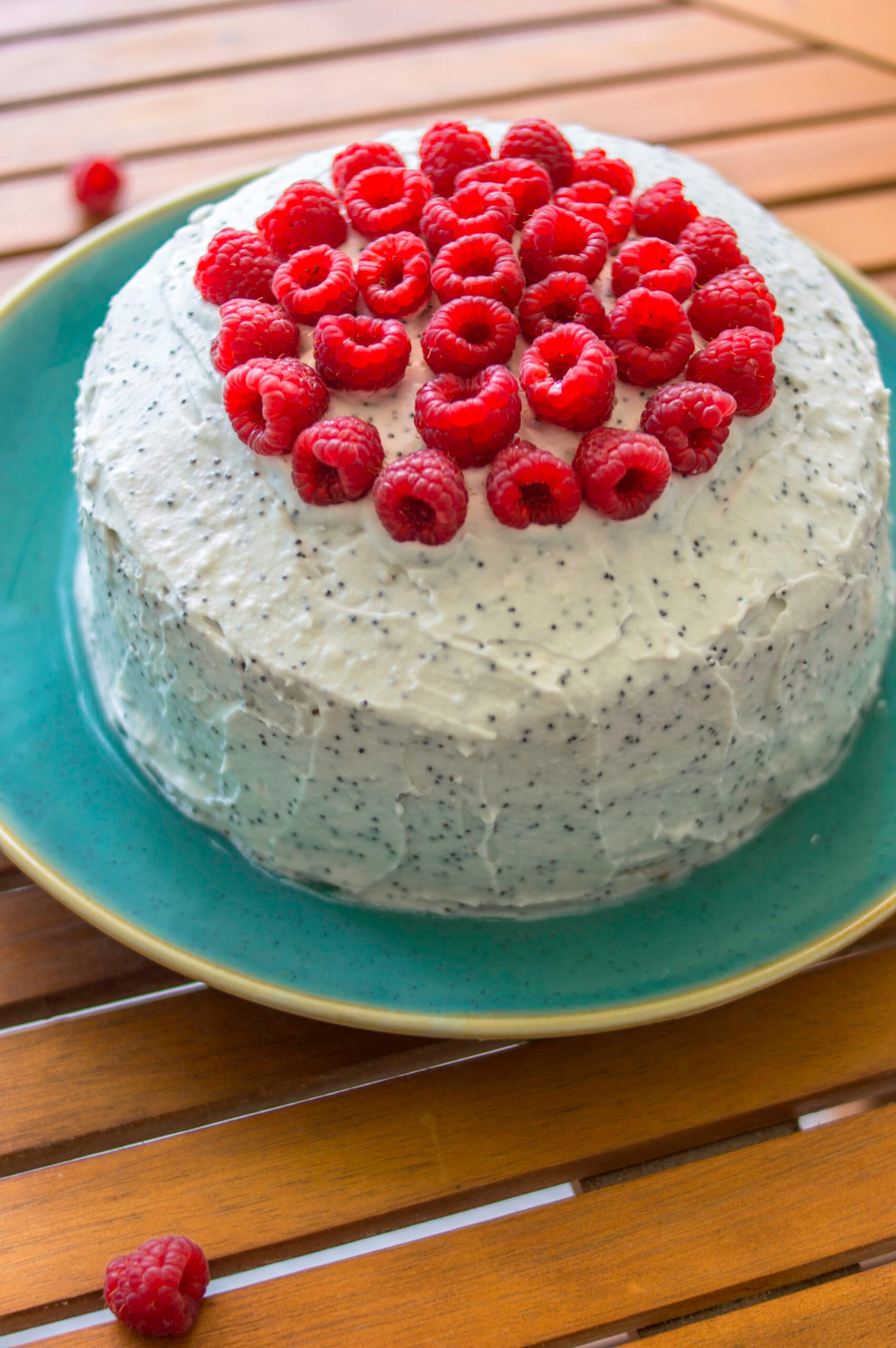 Slice of vegan raspberry poppy-seed cake topped with fresh berries and creamy white frosting