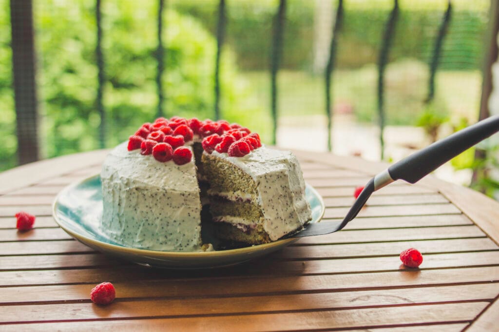 Slice of vegan raspberry poppy-seed cake topped with fresh berries and creamy white frosting