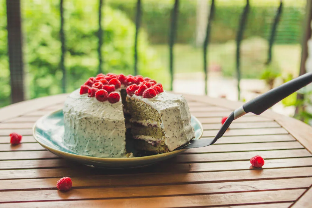 Slice of vegan raspberry poppy-seed cake topped with fresh berries and creamy white frosting
