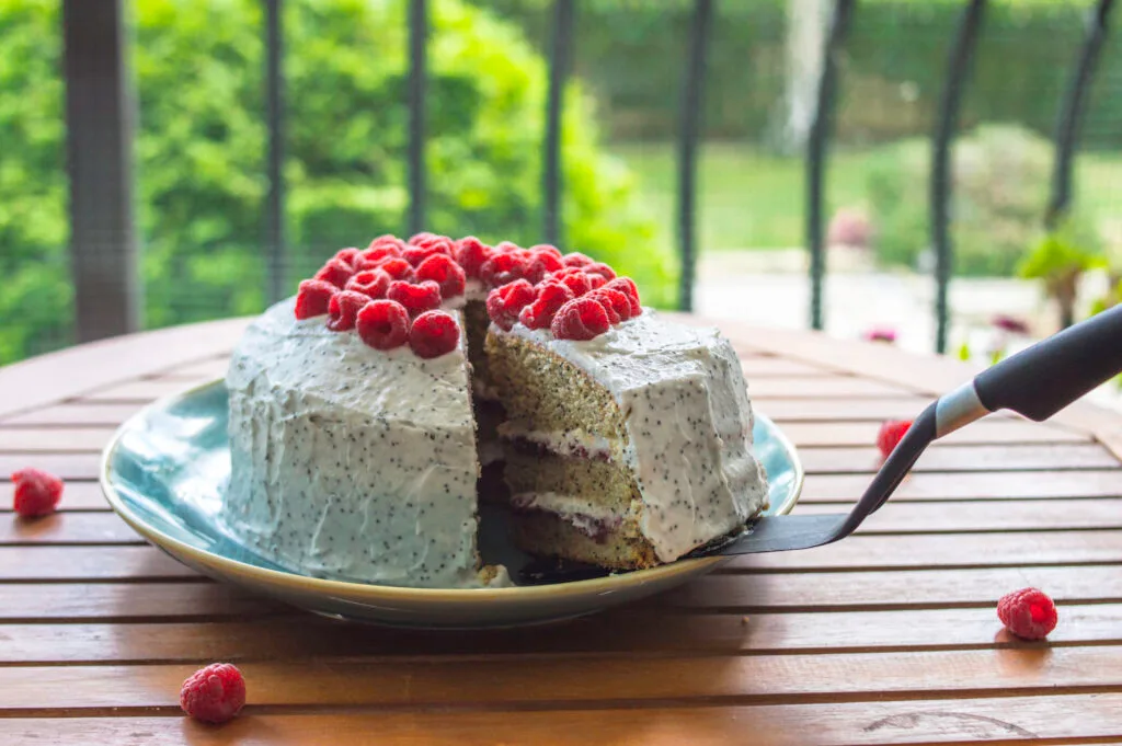 Slice of vegan raspberry poppy-seed cake topped with fresh berries and creamy white frosting