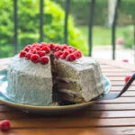 Slice of vegan raspberry poppy-seed cake topped with fresh berries and creamy white frosting