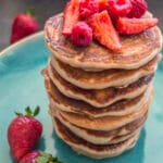 Stack of fluffy strawberry pancakes topped with syrup and fresh strawberries on a white plate