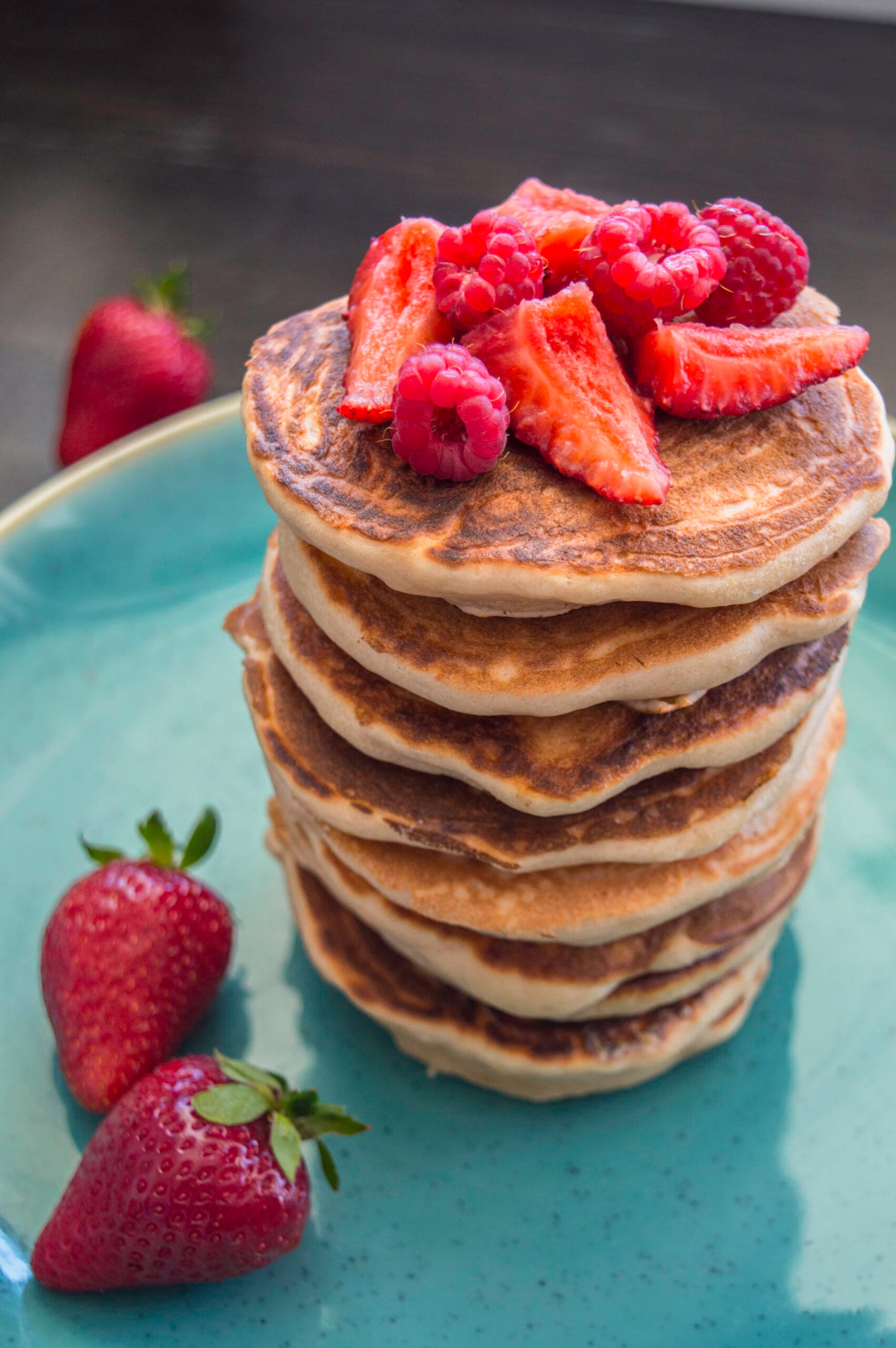 Stack of fluffy strawberry pancakes topped with syrup and fresh strawberries on a white plate
