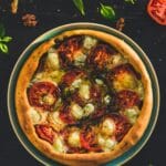 Rustic vegan tomato tart with golden crust, pesto base, and sliced tomatoes arranged in a circular pattern