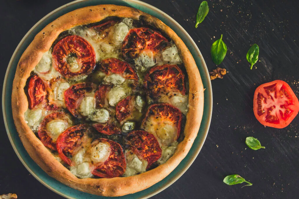 Rustic vegan tomato tart with golden crust, pesto base, and sliced tomatoes arranged in a circular pattern