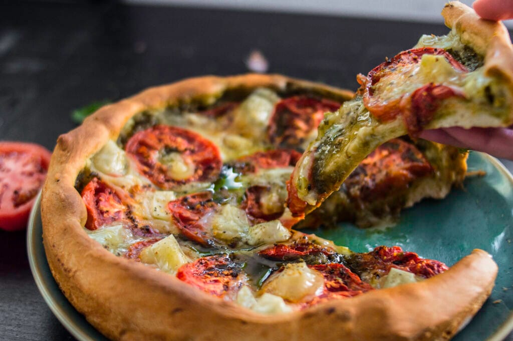 Rustic vegan tomato tart with golden crust, pesto base, and sliced tomatoes arranged in a circular pattern