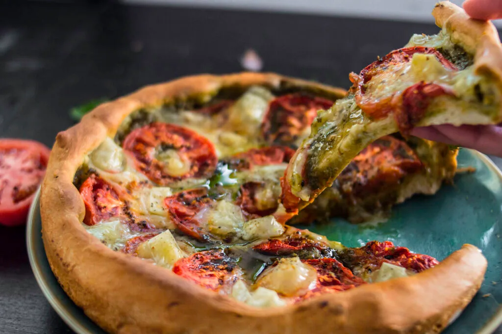 Rustic vegan tomato tart with golden crust, pesto base, and sliced tomatoes arranged in a circular pattern