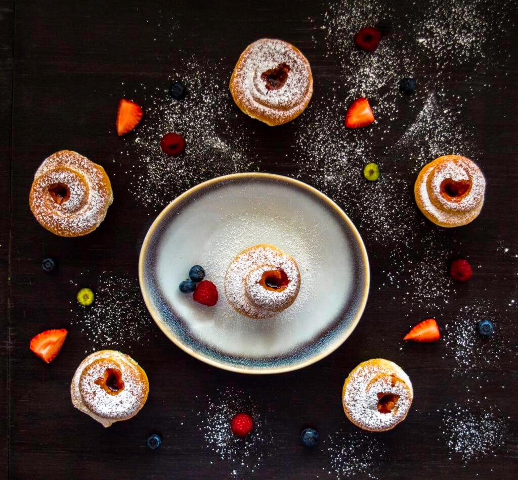 Flaky cruffins with powdered sugar and jam centers served in a muffin tin on a rustic table