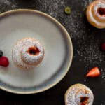 Flaky cruffins with powdered sugar and jam centers served in a muffin tin on a rustic table