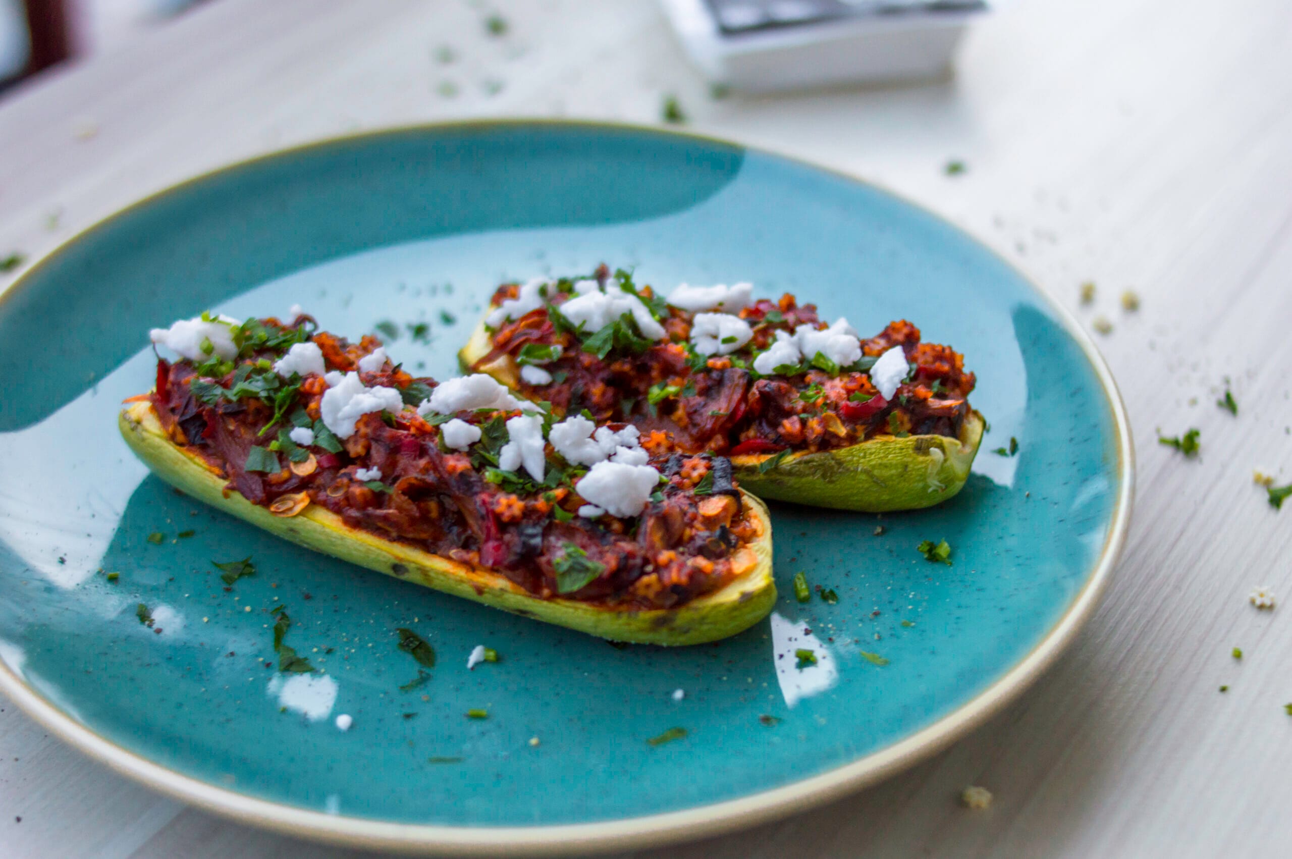 Baked zucchini halves stuffed with couscous tabbouleh mixture, topped with vegan white cheese and fresh parsley
