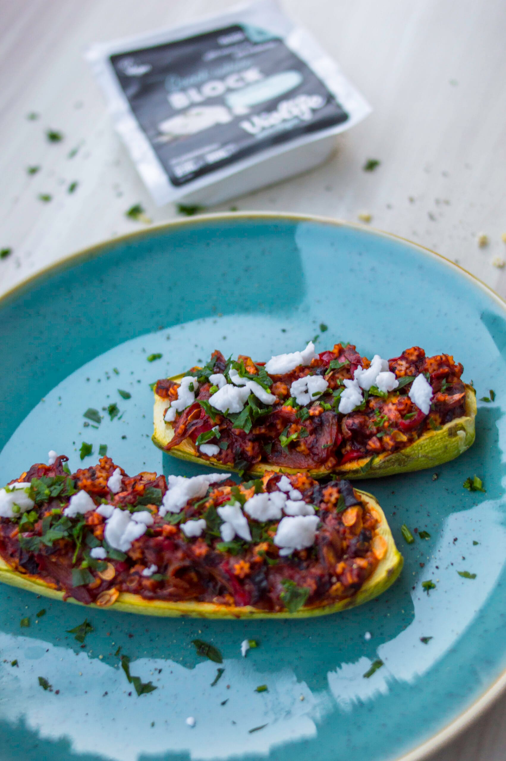 Baked zucchini halves stuffed with couscous tabbouleh mixture, topped with vegan white cheese and fresh parsley