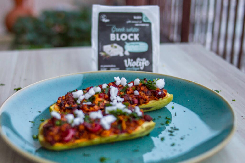 Baked zucchini halves stuffed with couscous tabbouleh mixture, topped with vegan white cheese and fresh parsley