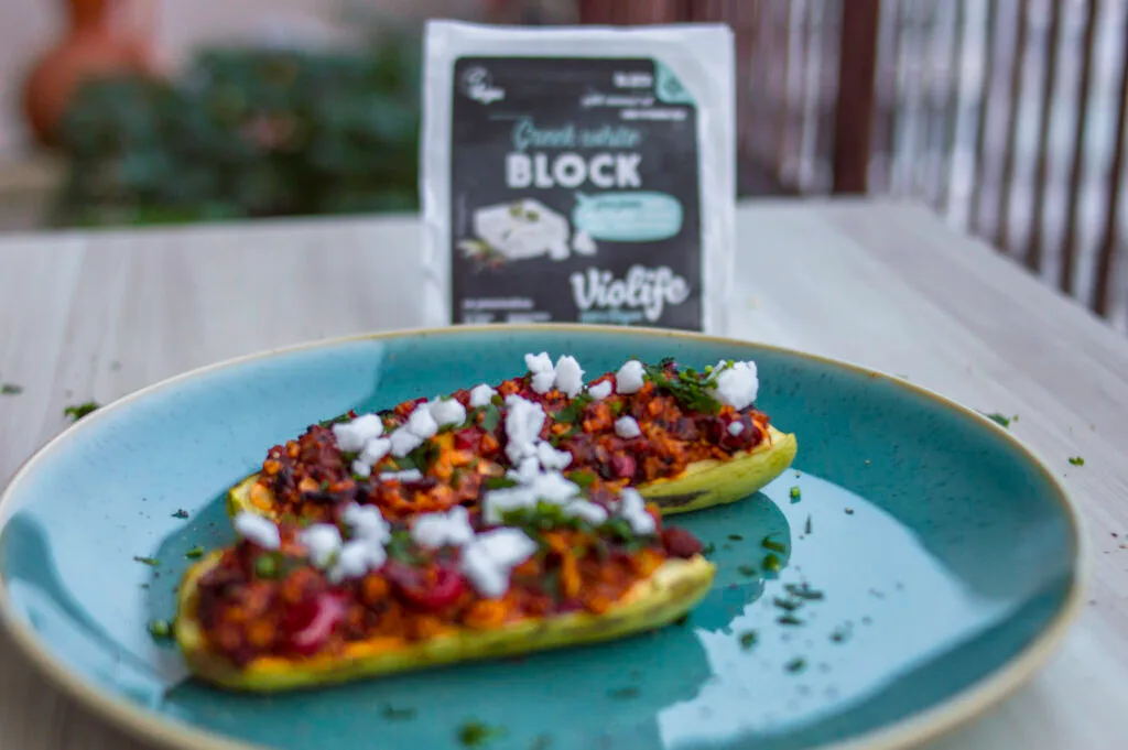 Baked zucchini halves stuffed with couscous tabbouleh mixture, topped with vegan white cheese and fresh parsley