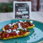 Baked zucchini halves stuffed with couscous tabbouleh mixture, topped with vegan white cheese and fresh parsley