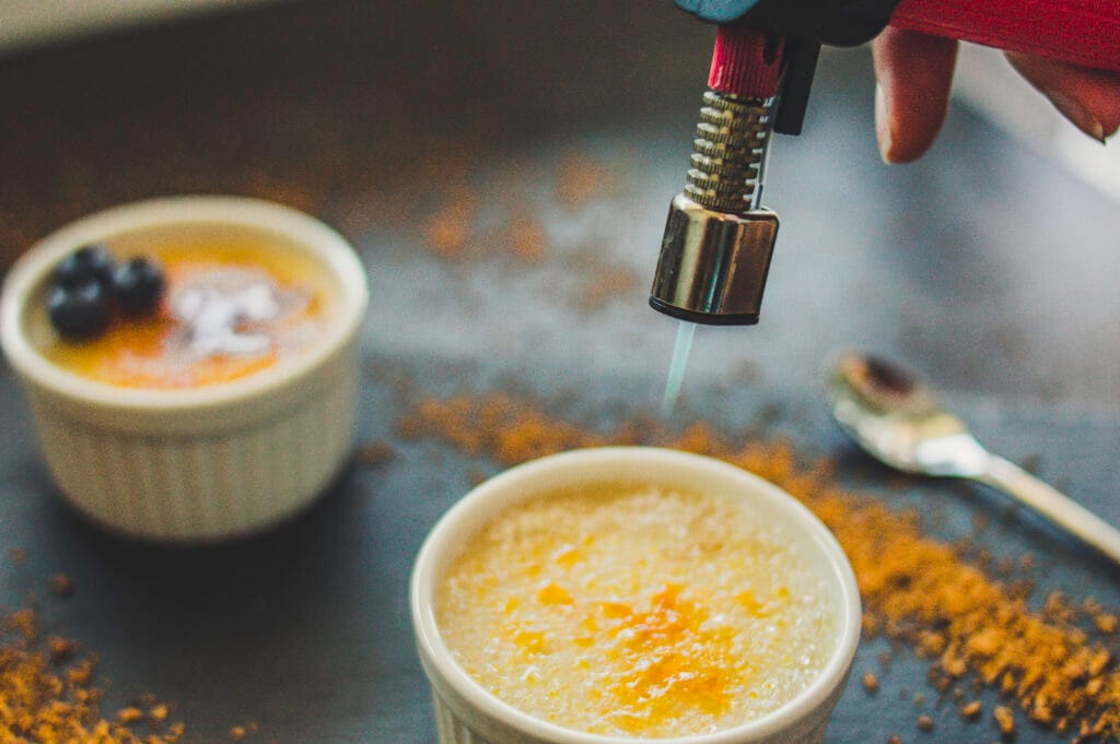 Small ramekin with vegan crème brûlée topped with a golden caramelized sugar crust and a vanilla pod beside it
