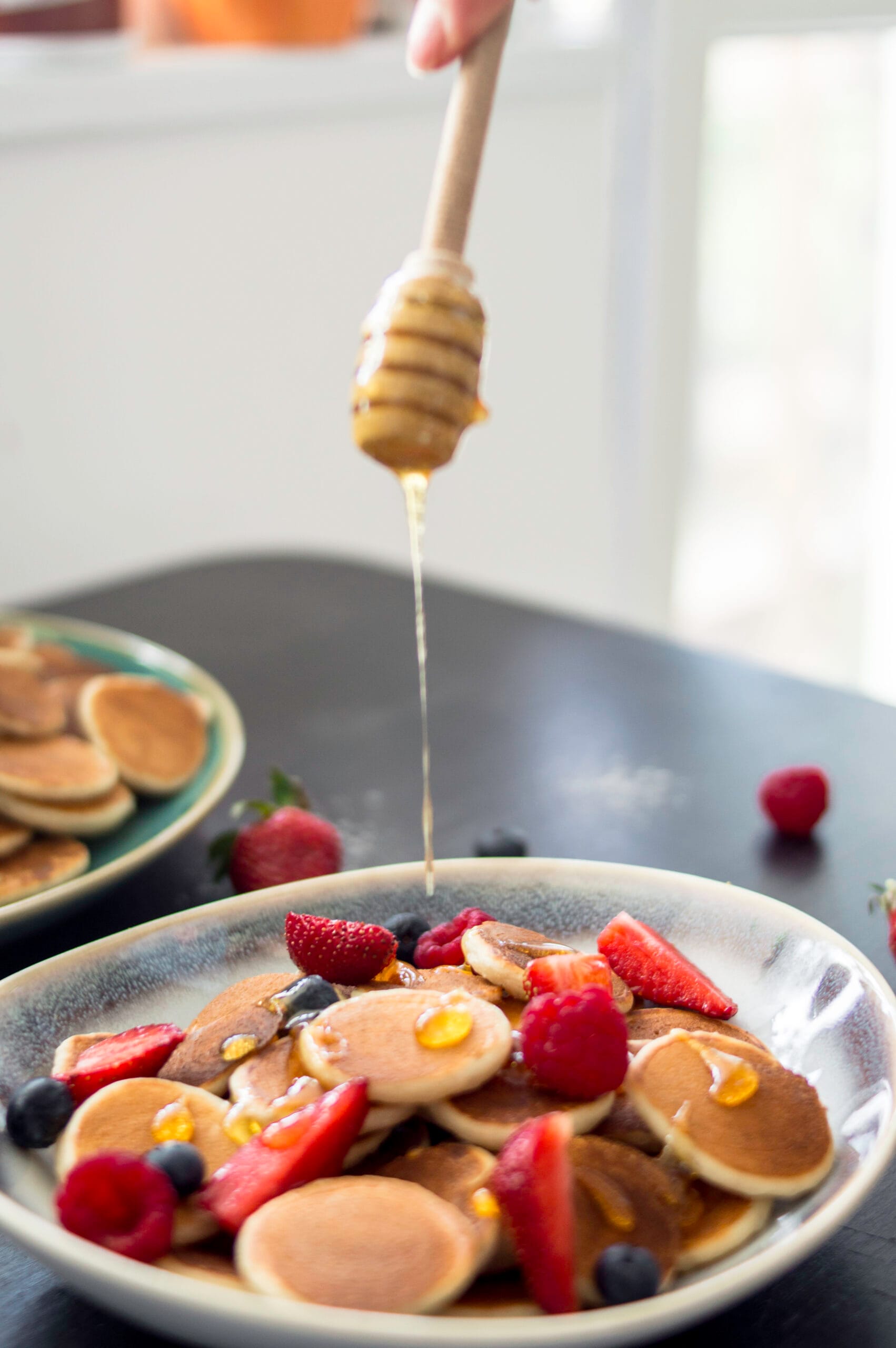 Bowl of golden mini pancakes (pancake cereal) topped with fresh fruit and maple syrup