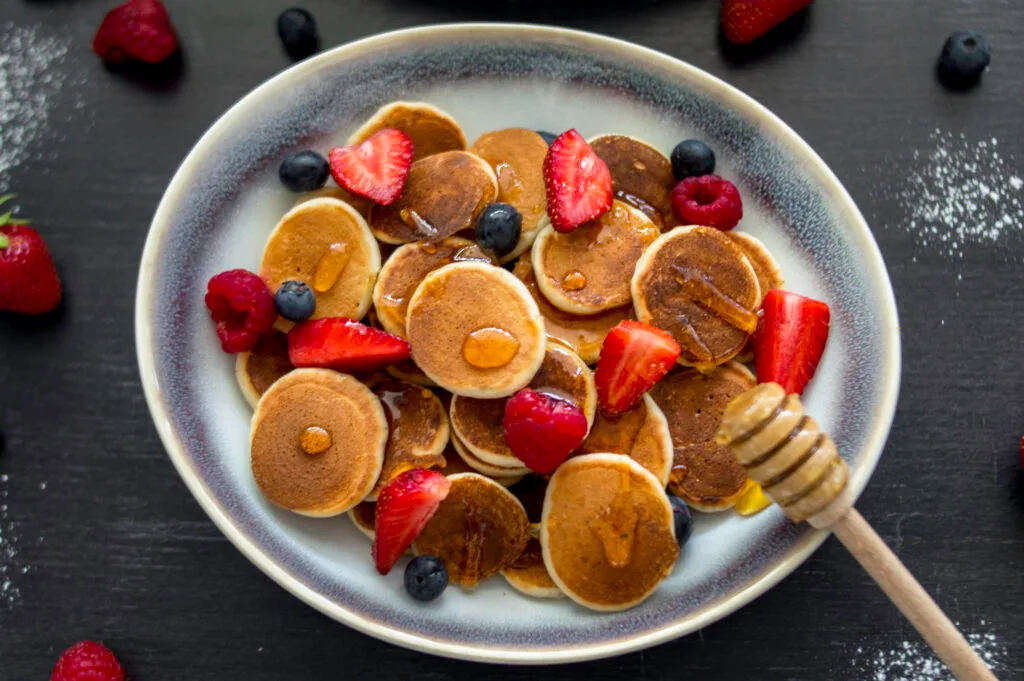 Bowl of golden mini pancakes (pancake cereal) topped with fresh fruit and maple syrup