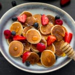 Bowl of golden mini pancakes (pancake cereal) topped with fresh fruit and maple syrup
