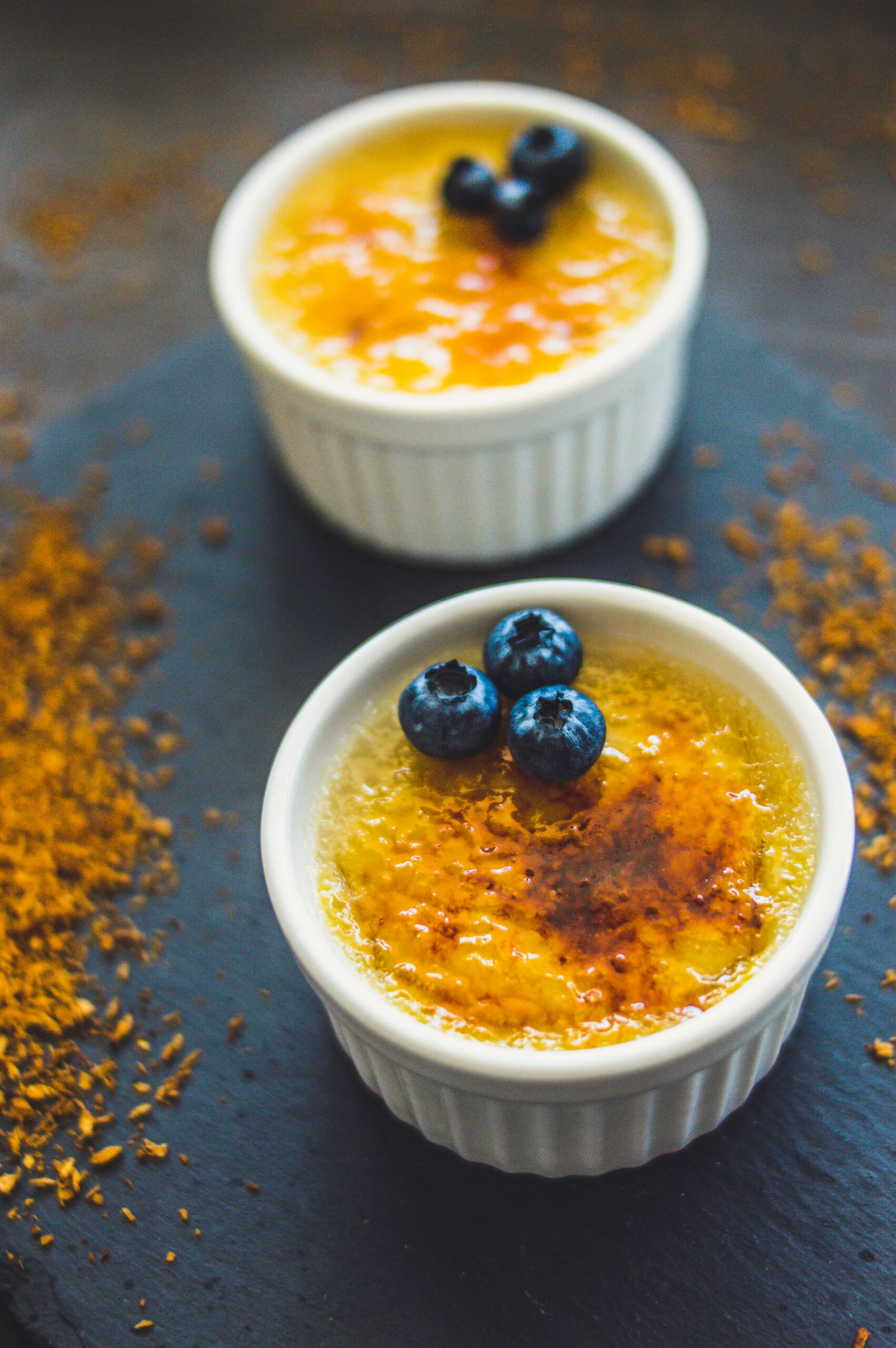 Small ramekin with vegan crème brûlée topped with a golden caramelized sugar crust and a vanilla pod beside it